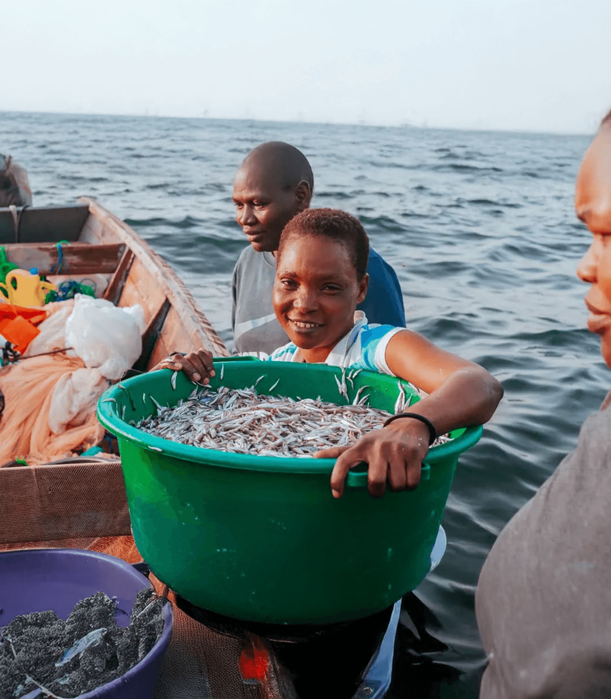 a lady holding a basket full of sardines with a water body in the background