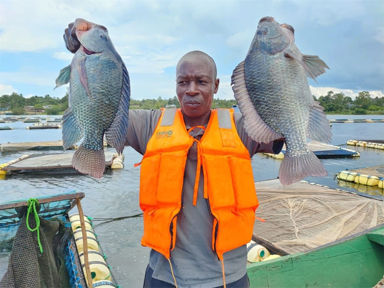 A man with an orange life jacket holding 2 fish
