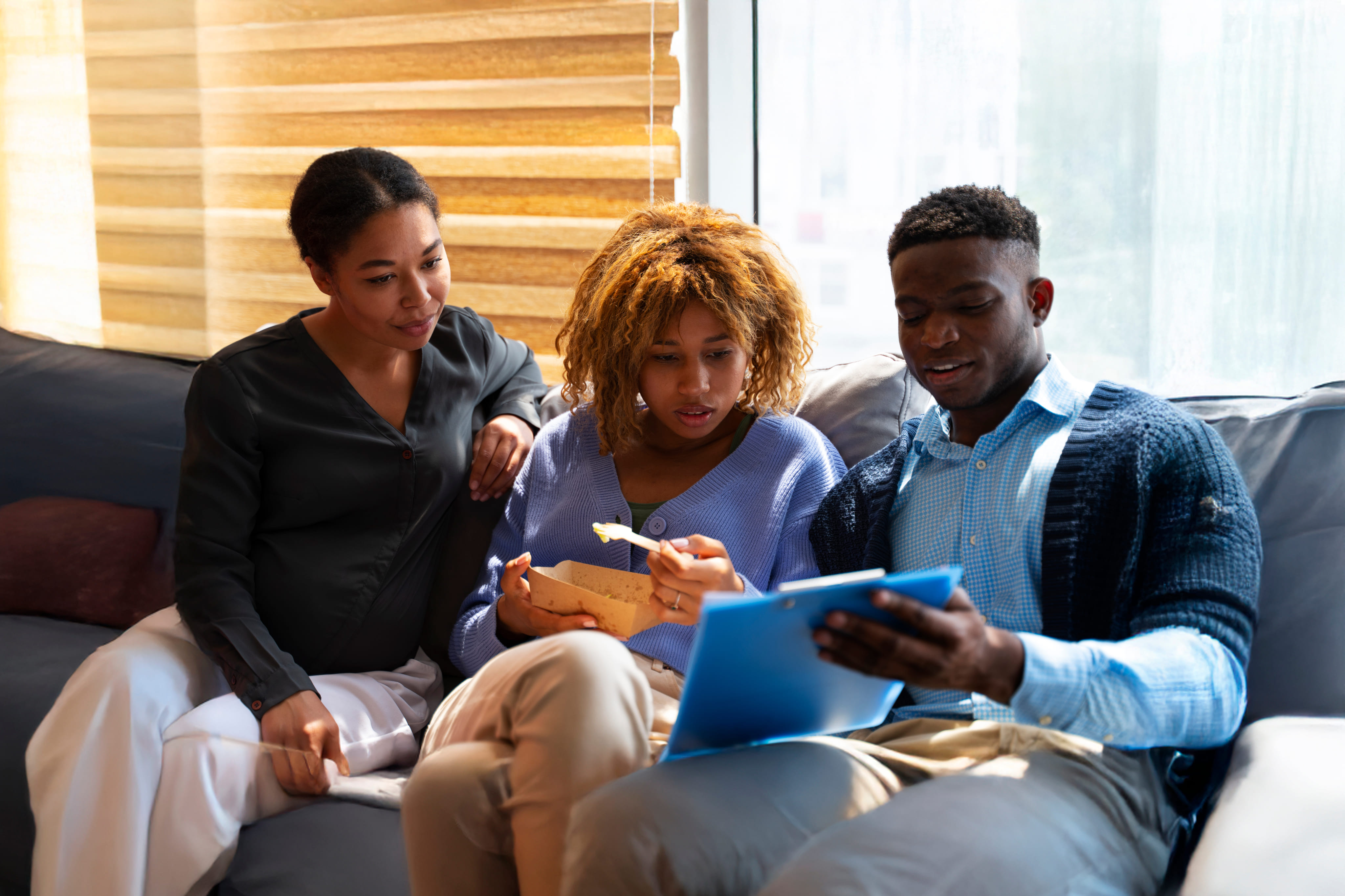 three people seated in a couch appearing to be discussing some content in a clipboard